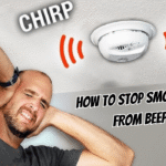 Frustrated man covering ears while smoke alarm beeps overhead — how to stop smoke alarm from beeping in the middle of the night